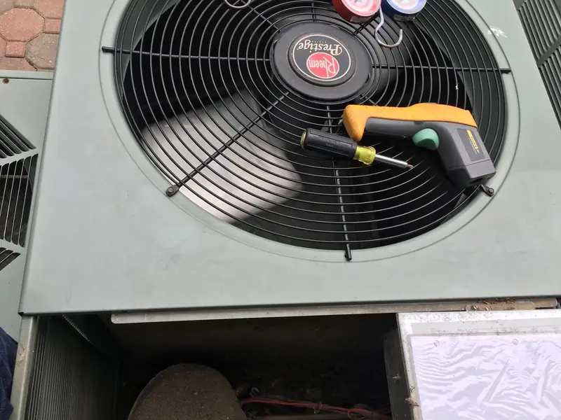 Rheem condenser fan guard with an infrared thermometer and screwdriver resting on it during a check