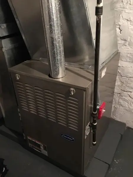 Gas furnace with a silver flue pipe and a red gas shut-off valve against an exposed brick wall