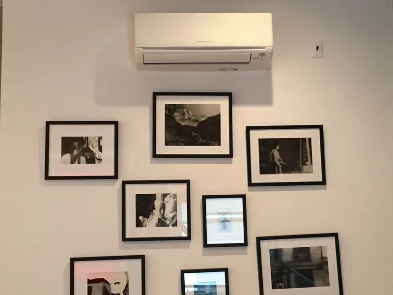 Ductless mini-split head mounted high on a wall above a group of framed black and white prints