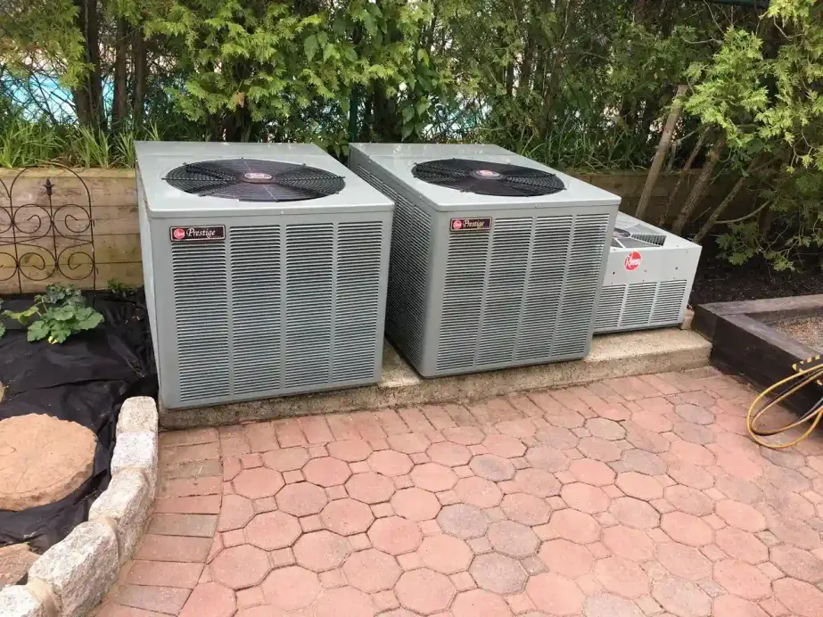 Two Rheem condensers on a brick patio with a manifold gauge hose attached